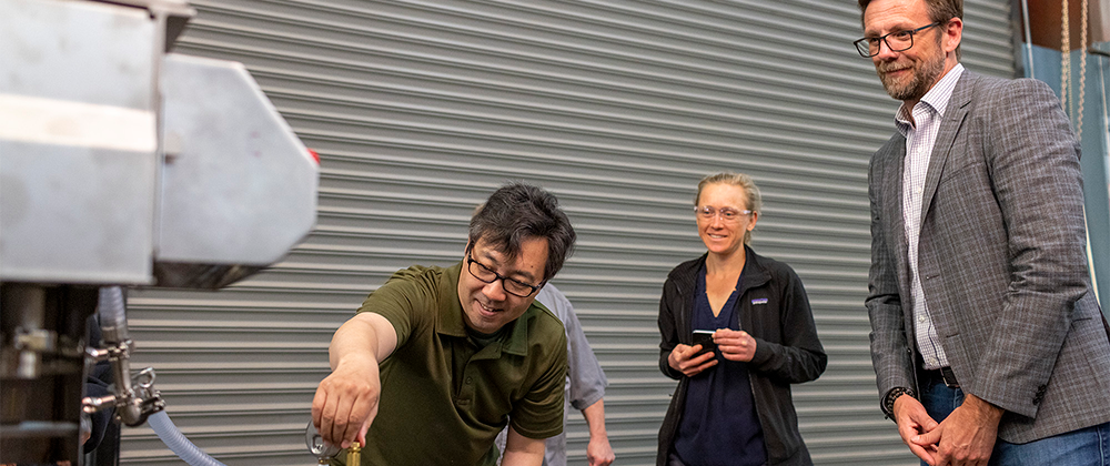 Employer with two employees testing equipment at manufacturing facility.